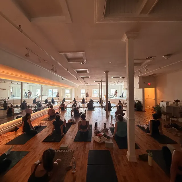 A full yoga class seated on mats across the main floor at golden hour